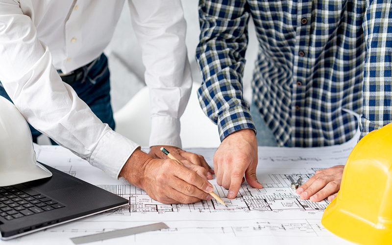 Architects reviewing a blueprint design to optimize landed house construction.