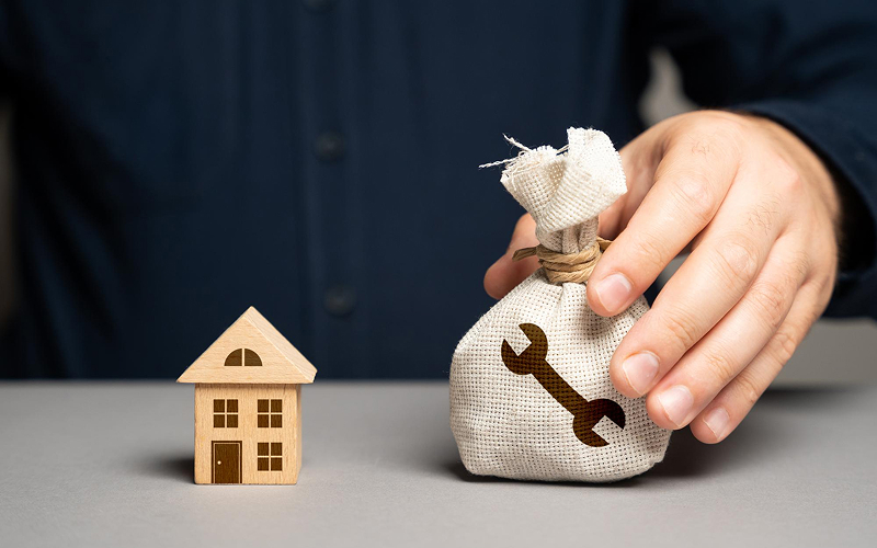Man holding a money bag next to a miniature house.